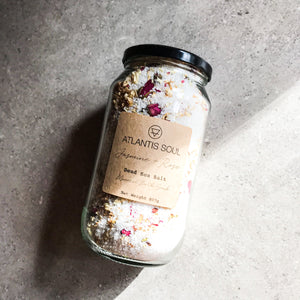 White Fine Mineral Salts in a glass jar with a black screw top lid with dried red rose buds and Jasmine flowers. 